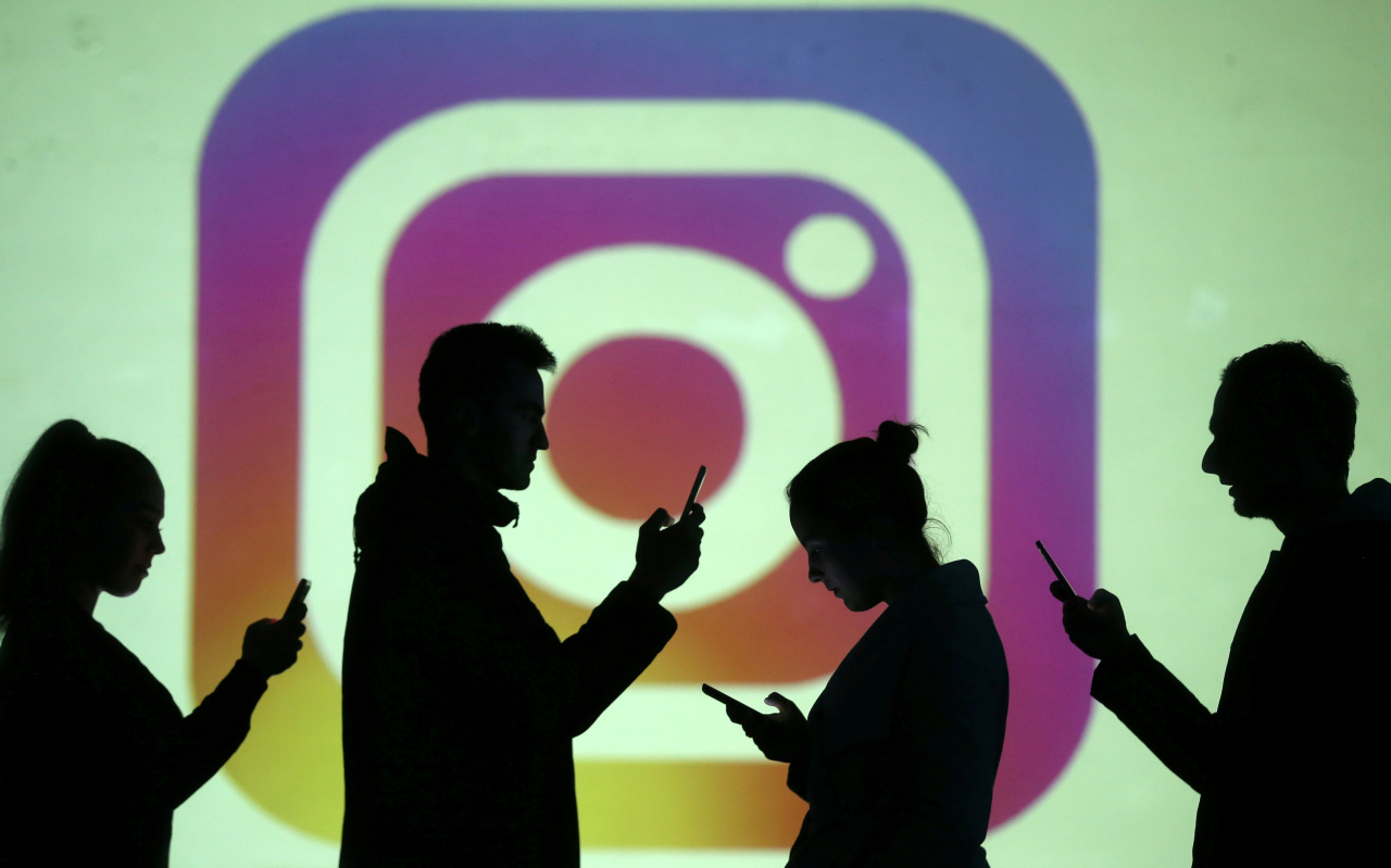 Silhouettes of mobile device users are seen next to a screen projection of Instagram logo (Reuters-Yonhap)