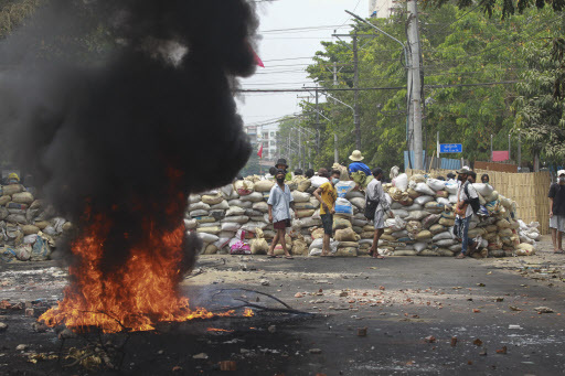 Anti-coup protesters stand beside a burning tire as they fortify their position against the military during a demonstration in Yangon, Myanmar on Tuesday March 30, 2021. (AP-Yonhap)