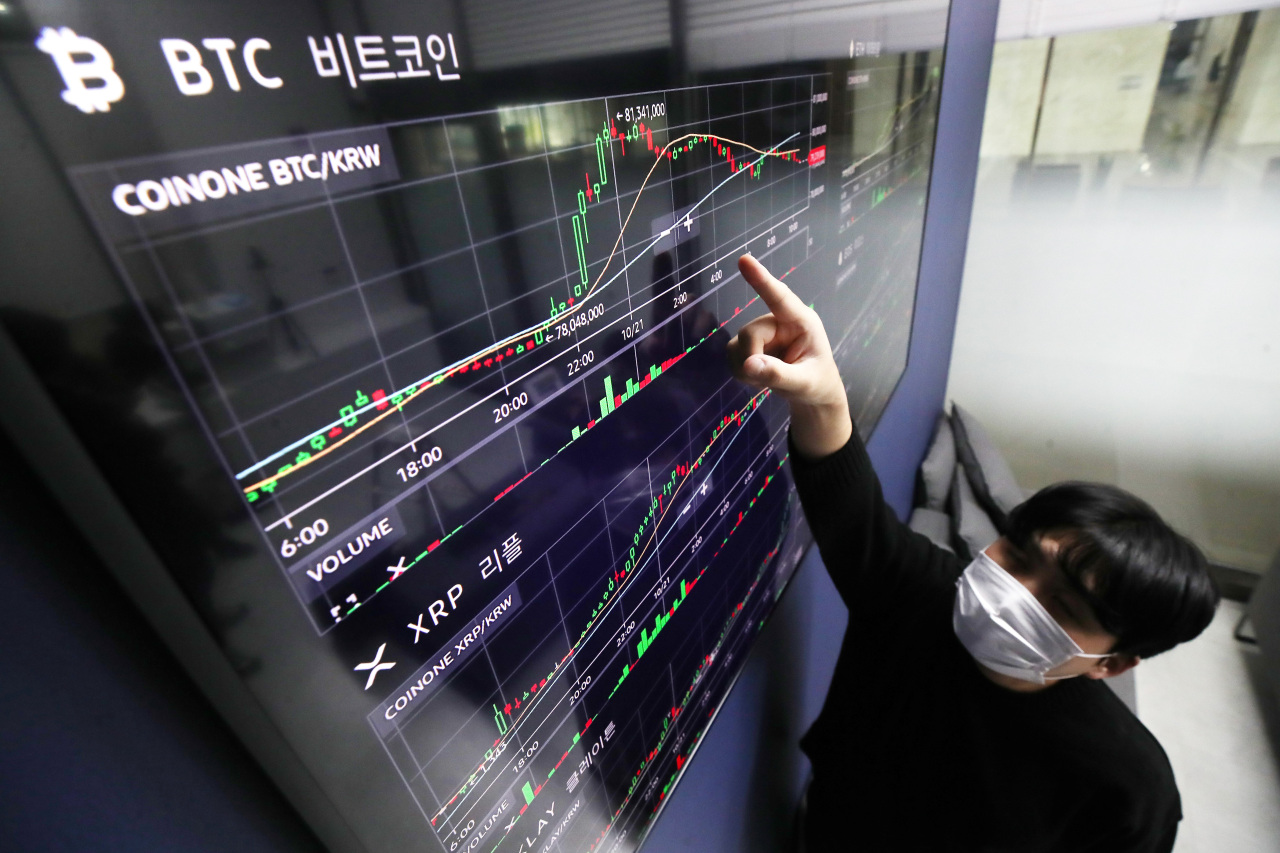 An employee of Coinone points at a digital board that shows the price movement of Bitcoin on Thursday. (Yonhap)