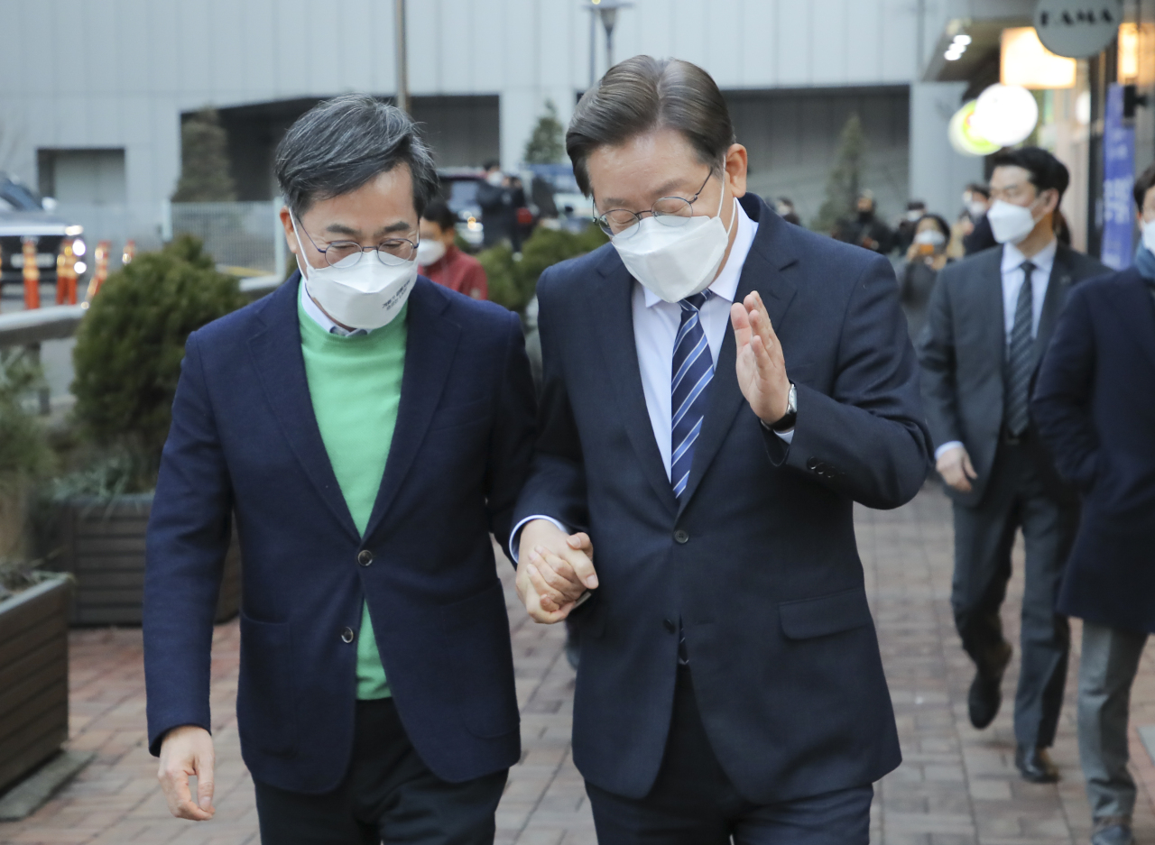 Presidential candidates Lee Jae-myung of the ruling Democratic Party of Korea (right) and Kim Dong-yeon, a nominee of the New Wave, walk together holding hands in Seoul on Tuesday. (Yonhap)