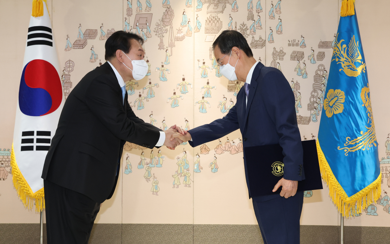 President Yoon Suk-yeol (left) shakes hands with Prime Minister Han Duck-soo after conferring an appointment certificate on Han at the presidential office in Seoul on Saturday. (Yonhap)