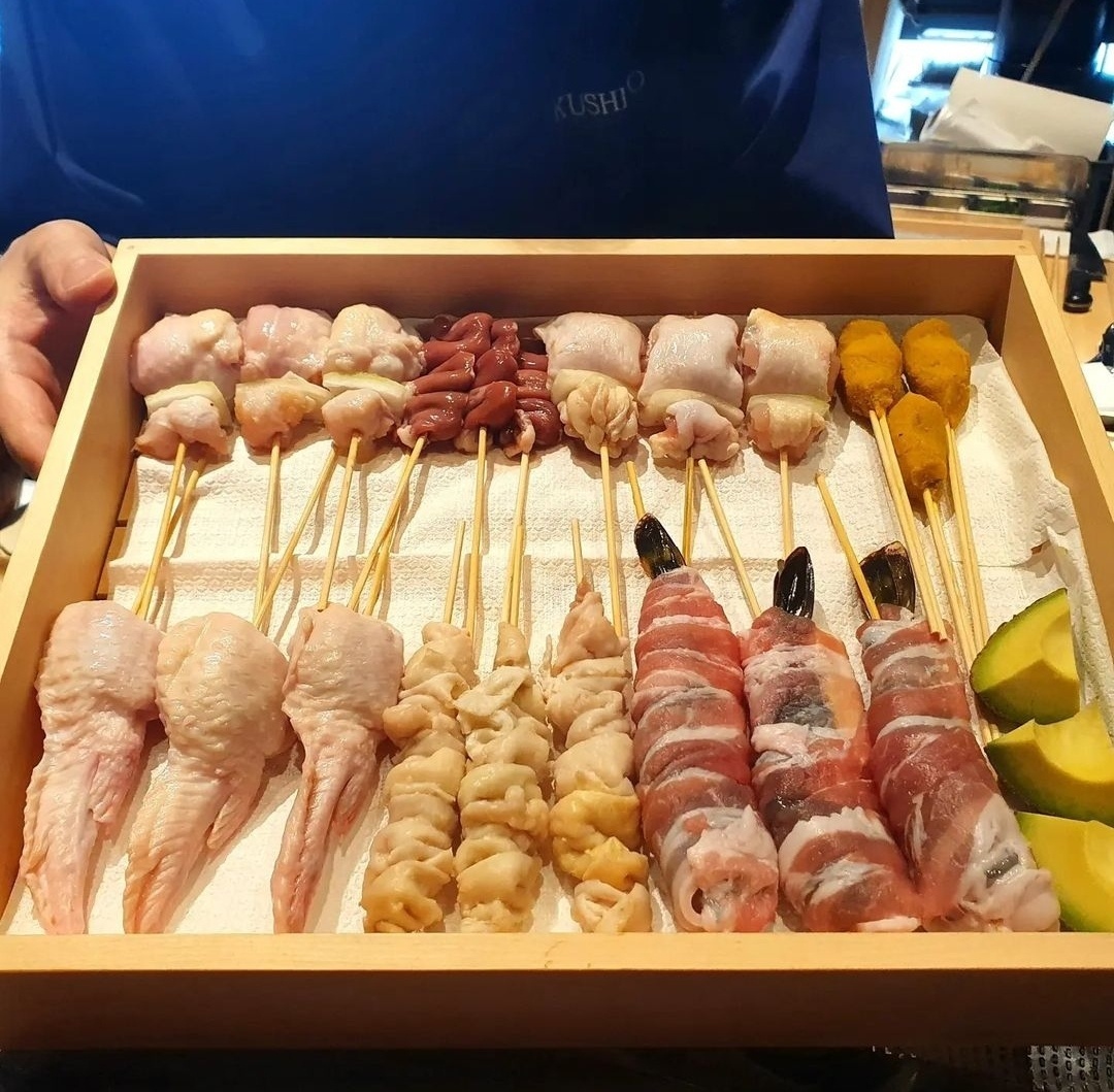 A chef holds a wood plate of raw chicken skewers before frying them at Kushiho (Kushiho)