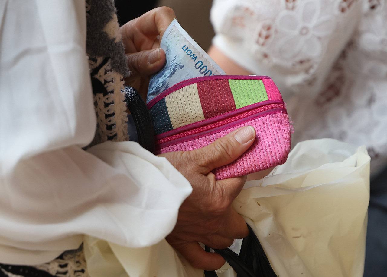 A consumer takes a 1,000-won bill out of her purse at a traditional market in Seoul on Friday. Consumer prices growth reached 5.4 percent in May 2022, while it stayed at 2.6 percent in May 2021 and minus 0.2 percent in May 2020. (Yonhap)