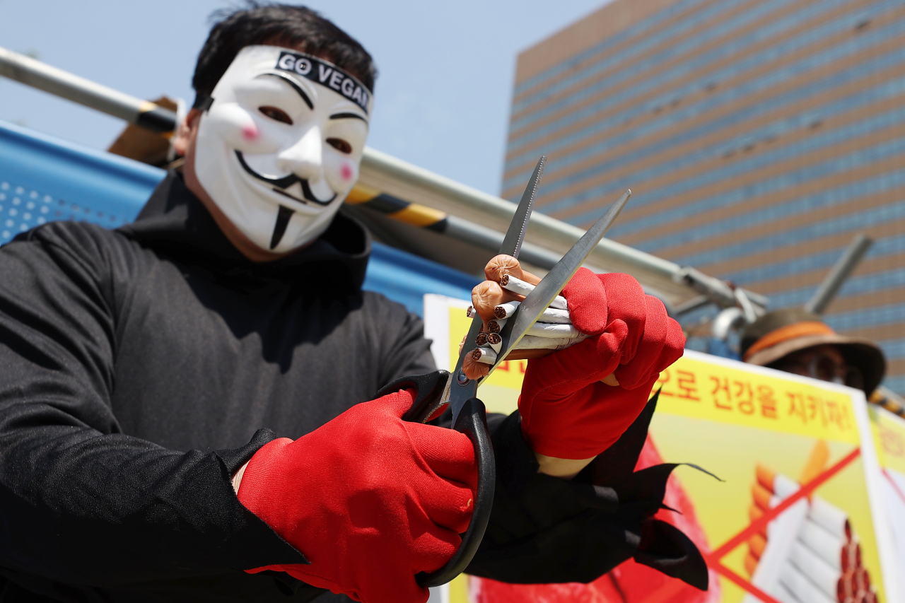 A member of the Korea Vegan Union cuts cigarettes and sausages as part of a demonstration urging people to quit smoking and go vegan in this May 31 file photo. (Yonhap)