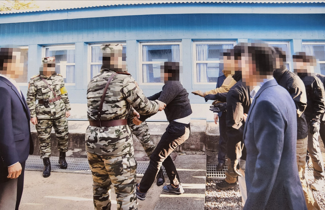 This photo, provided by the Ministry of Unification last Tuesday, shows a North Korean fisherman (C, in gray), who was captured near the eastern inter-Korean sea border, resisting as he is handed over to North Korean authorities in the inter-Korean truce village of Panmunjom in November 2019. (Ministry of Unification)