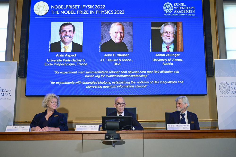 Secretary General of the Royal Swedish Academy of Sciences Hans Ellegren, centre, Eva Olsson, left and Thors Hans Hansson, members of the Nobel Committee for Physics announce the winner of the 2022 Nobel Prize in Physics, from left to right on the screen, Alain Aspect, John F. Clauser and Anton Zeilinger, during a press conference at the Royal Swedish Academy of Sciences, in Stockholm, Sweden Tuesday. (Jonas Ekstromer /TT News Agency via AP)