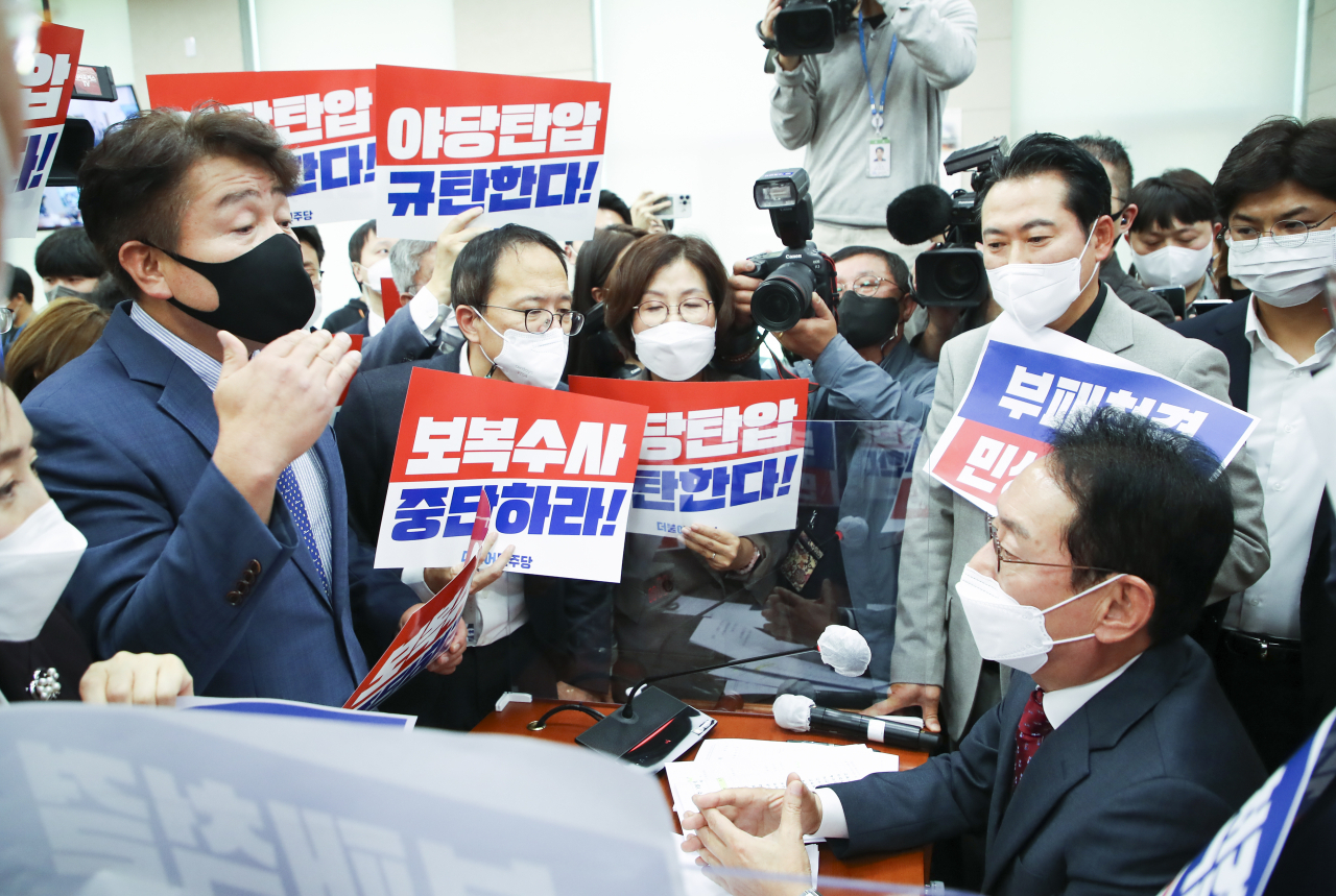 Lawmakers of the Democratic Party of Korea protest to legislative committee chairman Rep. Kim Do-eup (right) about launching a committee audit without mutual consent, Thursday. Banners read “Stop retaliatory investigation” and “We deplore the persecution of the opposition party.” (Yonhap)