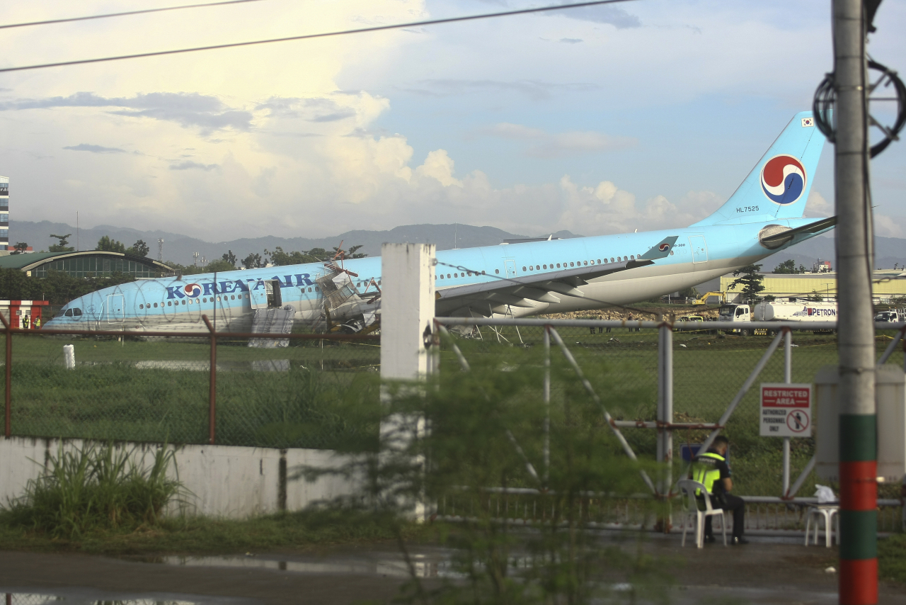 A security man keeps watch beside a damaged Korean Air plane after it overshot the runway at the Mactan-Cebu International Airport in Cebu, central Philippines early Monday Oct. 24, 2022. The Korean Air plane overshot the runway while landing in bad weather in the central Philippines late Sunday, but authorities said all 173 people on board were safe. (AP-Yonhap)