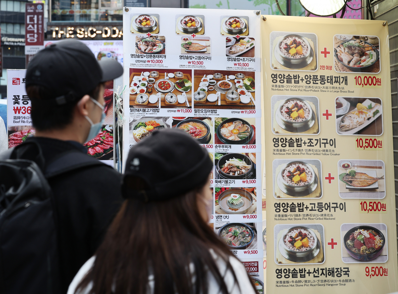 Citizens walk by standing signs of a restaurant menu in Seoul on Oct. 10. (Yonhap)