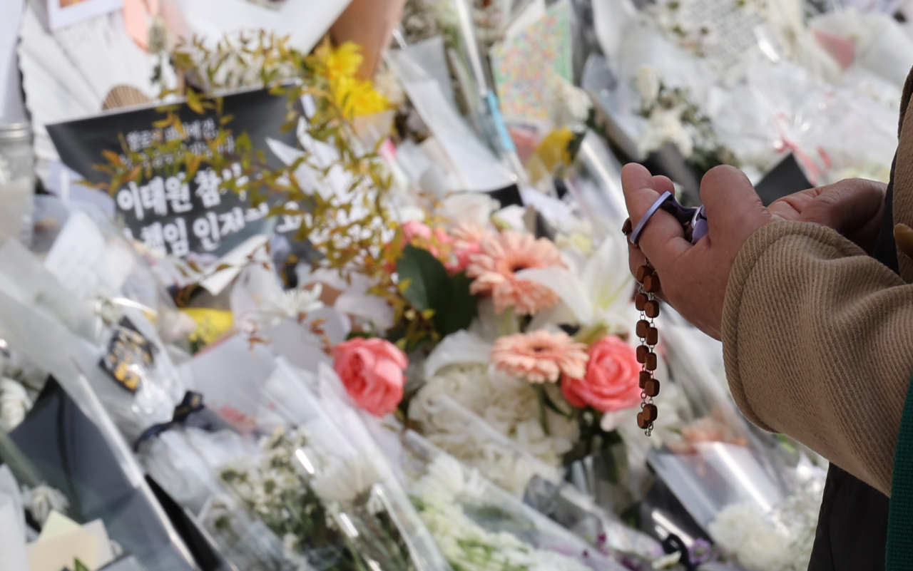 A passerby prays for the victims of Itaewon disaster in front of the flowers and messages at Itaewon Station, in Seoul, Monday. The national mourning period ended on Saturday, but grieving continues. (Yonhap)
