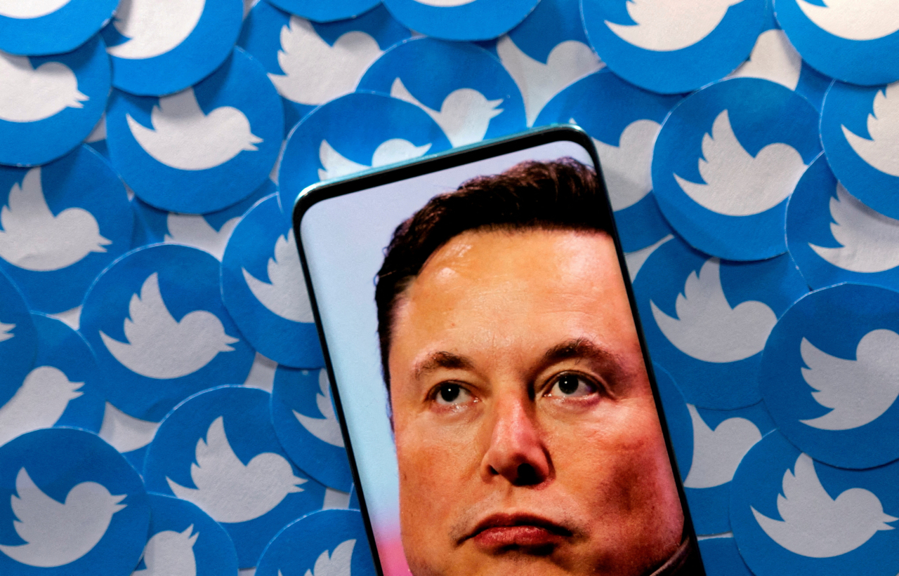 An image of Elon Musk is seen on a smartphone placed on printed Twitter logos in this picture illustration taken April 28, 2022. (Reuters-Yonhap)