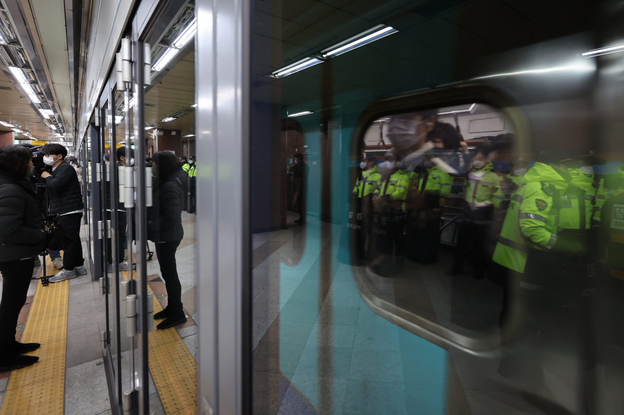 Yellow-vested police officers line up in front of a subway station's platform screen doors as a disabled activist group stages its rush-hour subway protest on Tuesday. (Yonhap)
