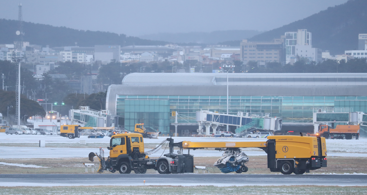 Snow removal vehicles clear snow from the runway of Jeju International Airport on Friday morning after heavy snow hit Jeju Island overnight. (Yonhap)