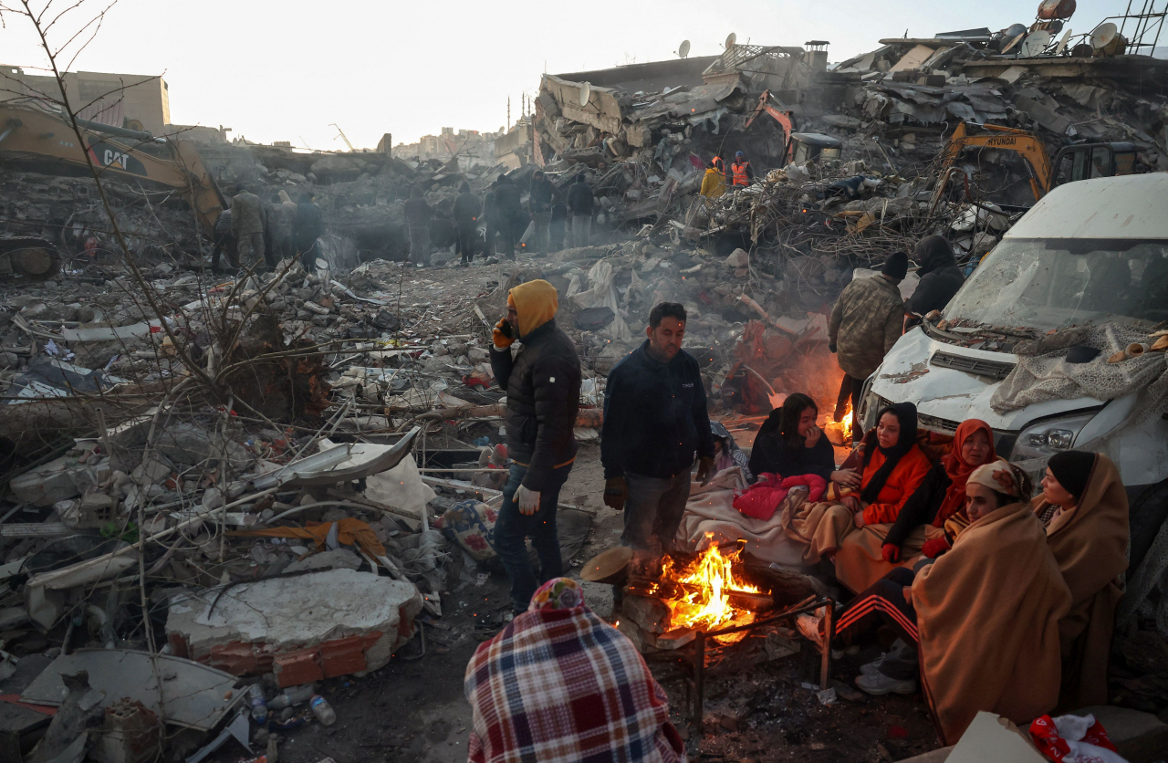 Survivors gather next to a bonfire outside collapsed buildings in Kahramanmaras on Wednesday, after their homes were destroyed in a 7.8 magnitude earthquake which struck the border region of Turkey and Syria on Monday. (AFP)