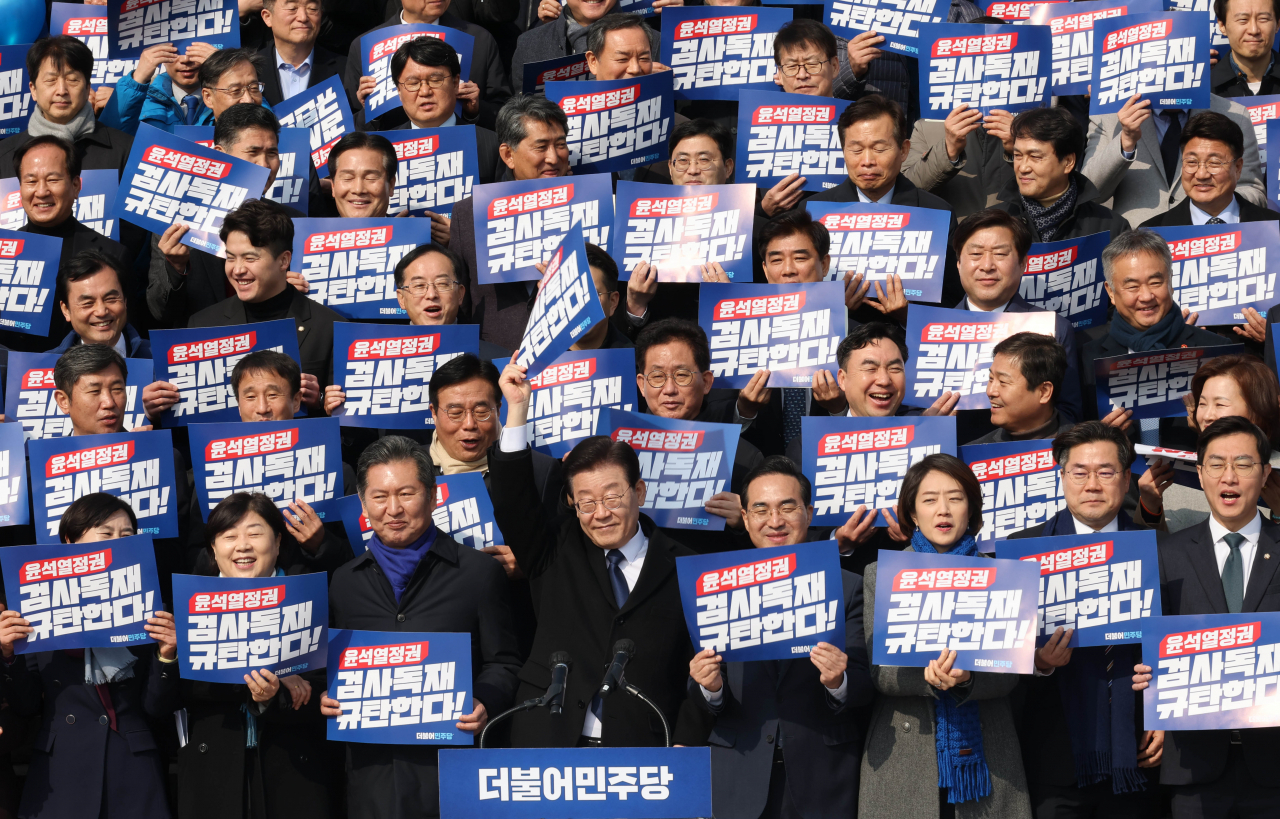 Lee Jae-myung (front row, fourth from left), chairman of the Democratic Party of Korea, raises his hand to greet at the rally to criticize Yoon Suk Yeol regime and prosecution held in front of the National Assembly's main office, Friday. Lawmakers and party officials at the rally are holding a hand sign that reads, 