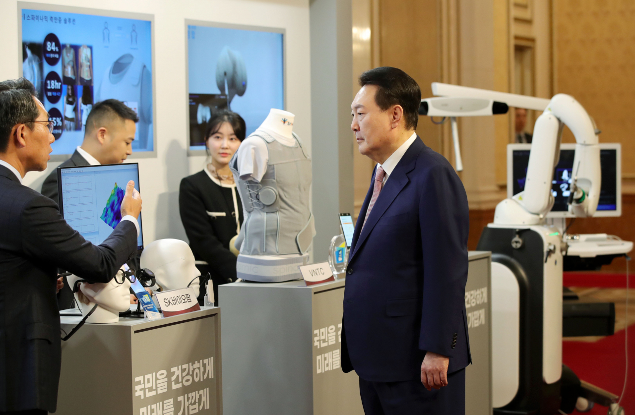 President Yoon Suk Yeol looks at SK Biopharmaceuticals' epilepsy-detecting wearable device prior to a biohealth market creation strategy meeting held at Cheong Wa Dae on Tuesday. (Yonhap)