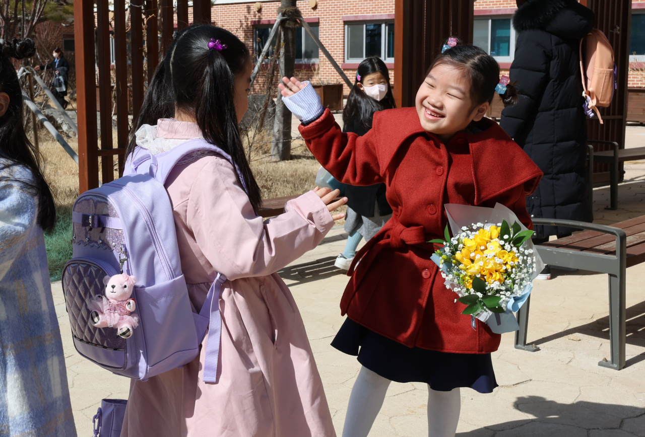 A no-masked grade one student greets her peer on Thursday, the first day of school. (Yonhap)