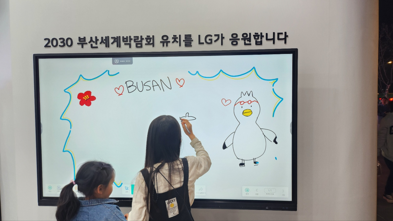 Children draw pictures of Busan Expo's mascot Boogie and write phrases supporting Busan's bid to host the 2030 World Expo on LG Interactive Digital Board, in LG Electronics' booth in Gwanghwamun Plaza, central Seoul, Sunday. (Lee Jung-youn/The Korea Herald)