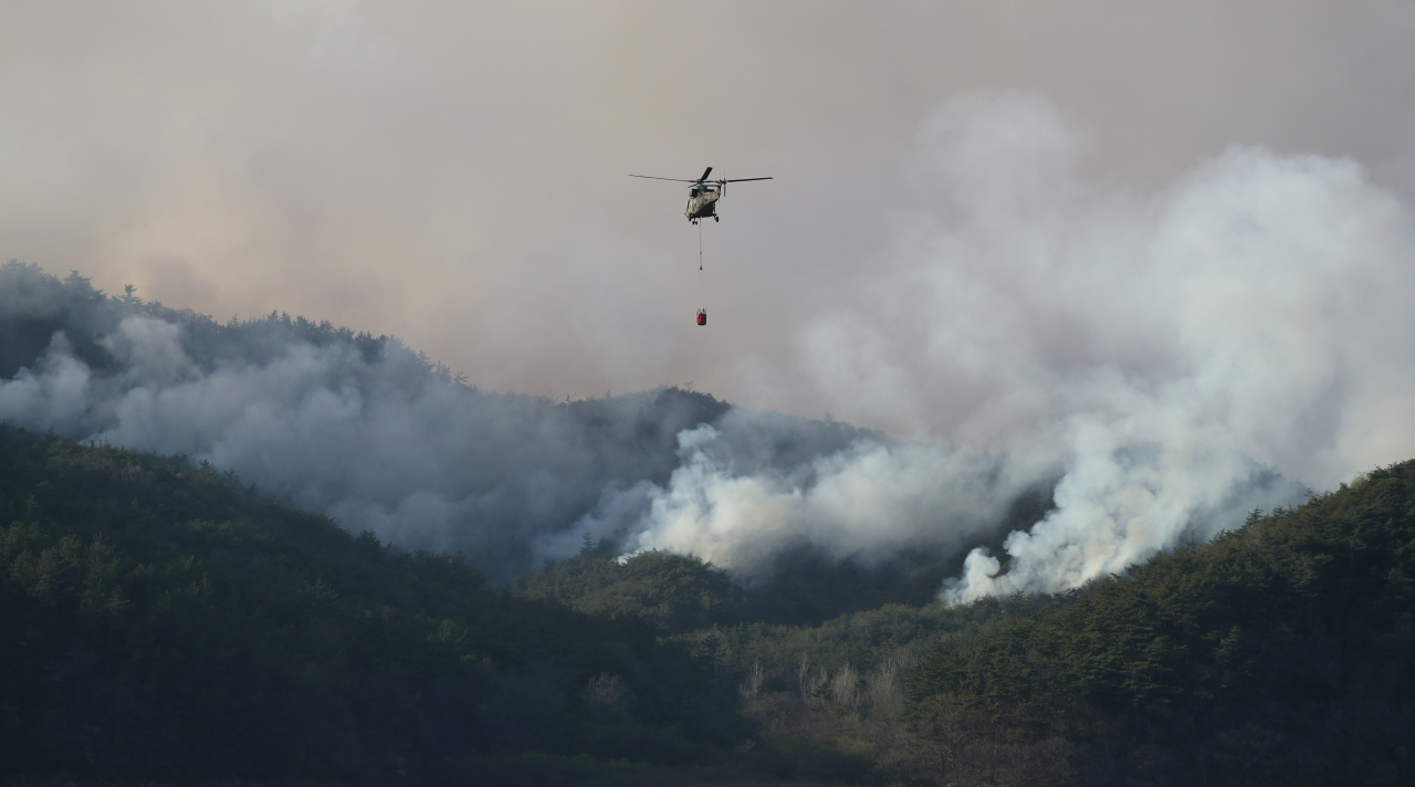 A National Fire Service helicopter flies over smoke from a fire in Hampyeong, South Jeolla Province on Monday, in a forest fire containment operation. (Yonhap)