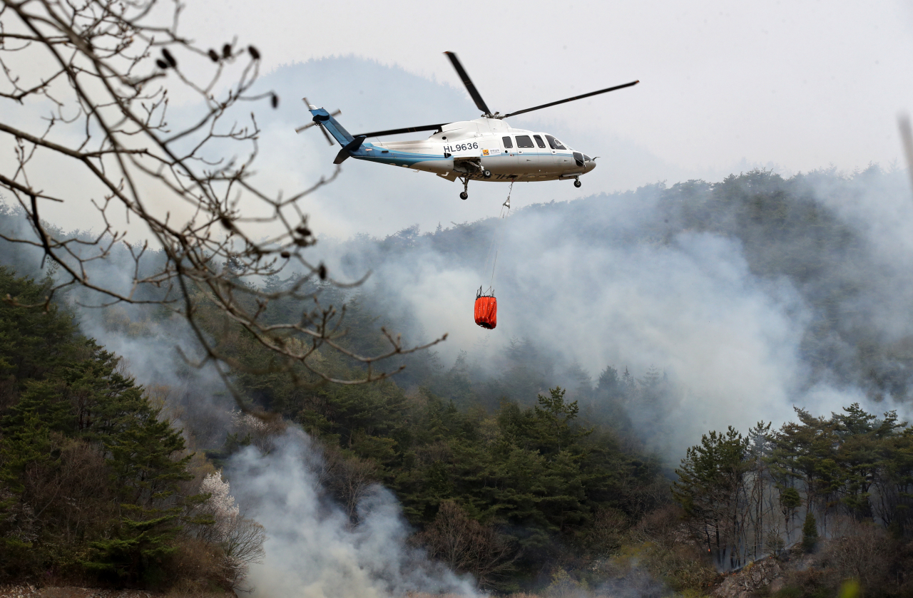 A chopper sprays water on a hill in Hongseong, South Chungcheong Province, Tuesday, where a wildfire has continued for the third day. (Yonhap)