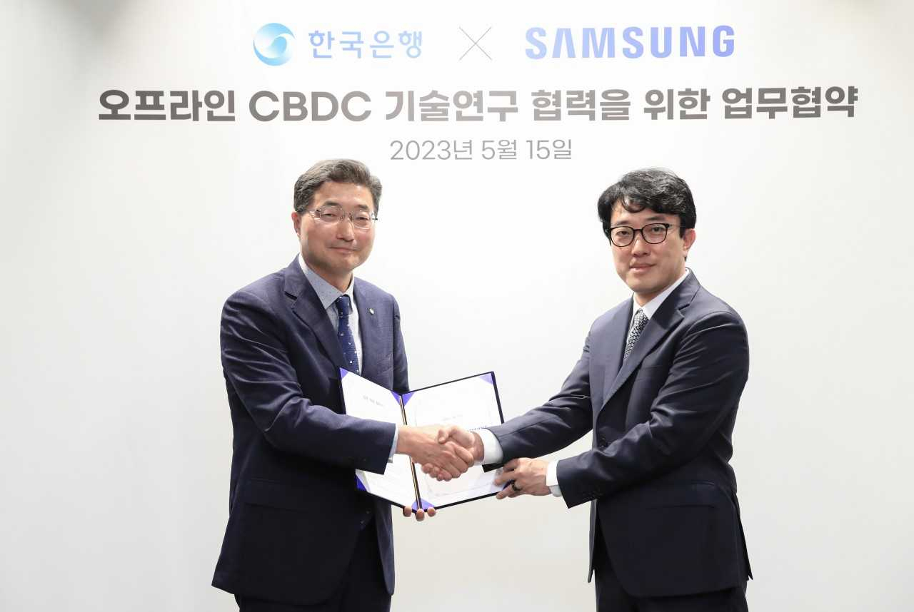 Bank of Korea Deputy Governor Lee Seung-heon (left) and Choi Won-joon, executive vice president and head of the mobile research and development office at Samsung’s Mobile eXperience division, pose for photos after signing a memorandum of understanding at Samsung’s headquarters in Suwon, Gyeonggi Province, Monday. (Bank of Korea)