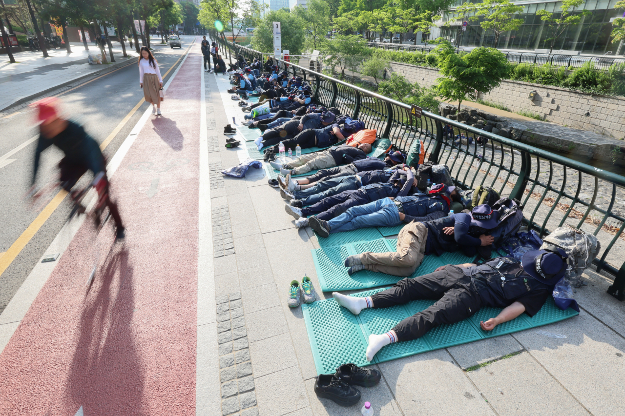 Citizens pass by KCTU construction union members who rest after participating in the general strike the previous night at Cheonggye Plaza in Jung-gu, Seoul, on May 17. (Yonhap)
