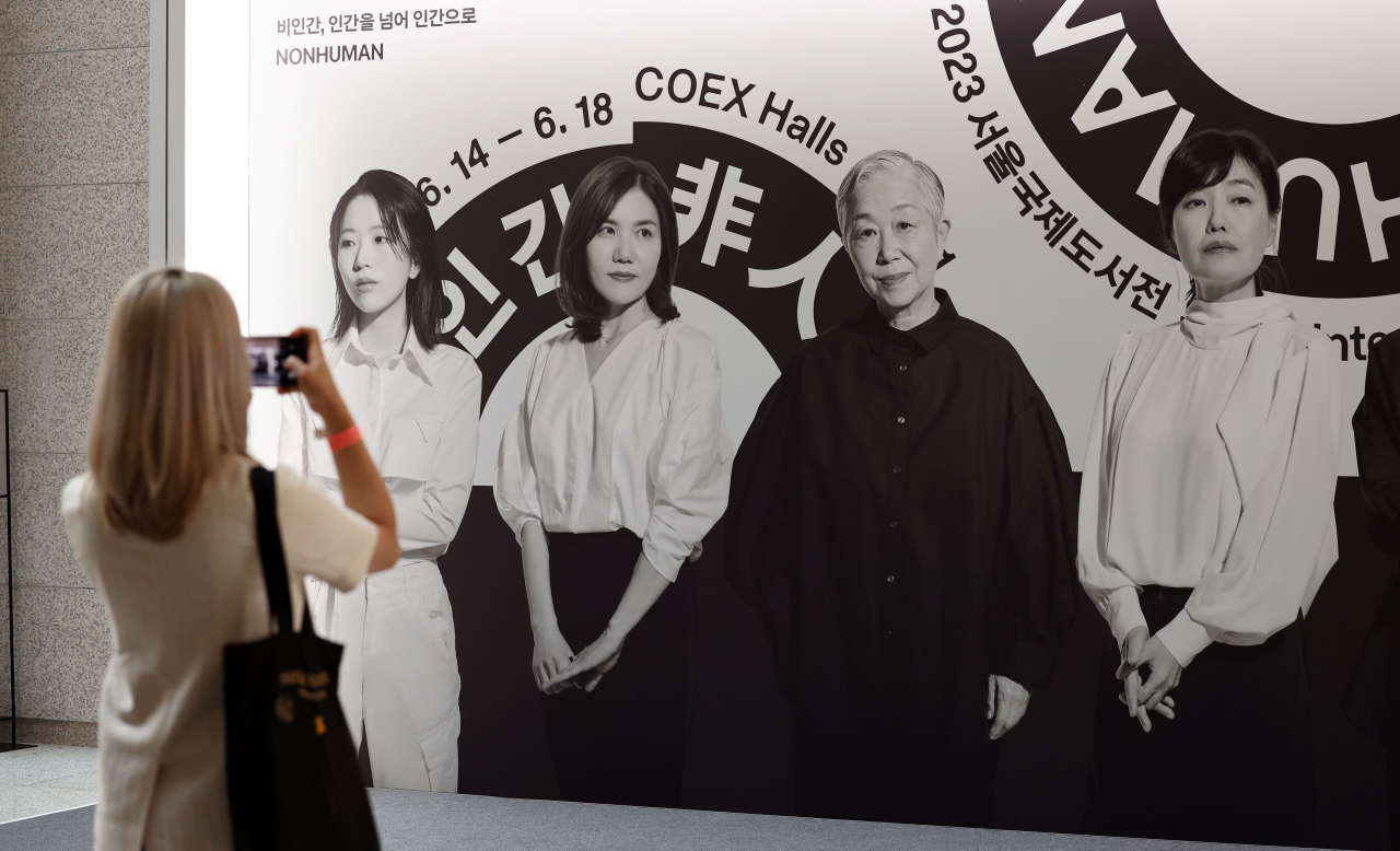 A visitor takes a photo of the poster showing the six promotional ambassadors for the 2023 Seoul International Book Fair, held at Coex in Gangnam-gu, southern Seoul, on Wednesday. Oh Jeong-hui is third from left in the poster. (Yonhap)