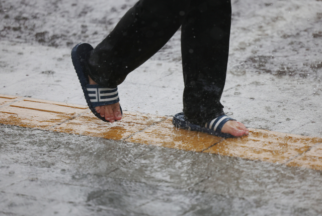 A person walks in the rain wearing plastic sandals. (Yonhap)