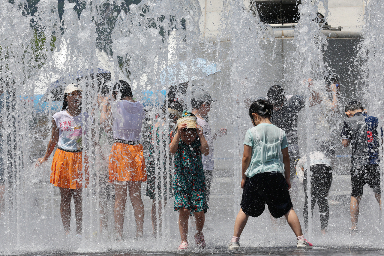 Children enjoy playing in the water at the fountain of Gwanghwamun Square, as heat wave warnings were issued throughout Seoul, Sunday. (Yonhap)