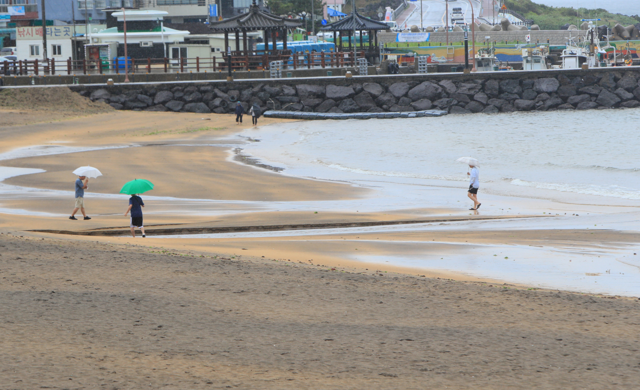 People holding umbrellas walk along a beach in Jeju on Sunday. (Yonhap)