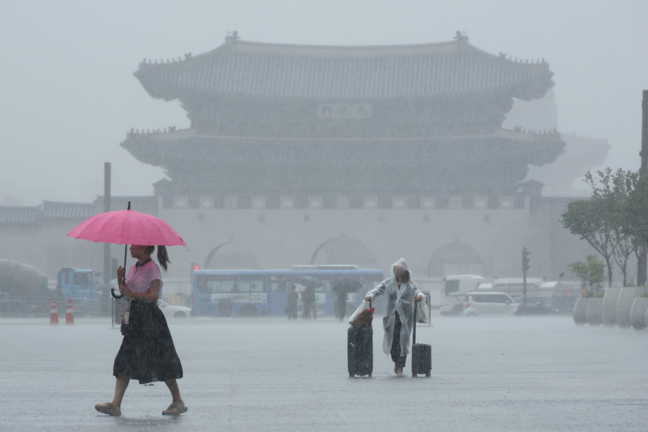 Passersby walk past Gwanghwamun in central Seoul amid heavy rain on Thursday. (Yonhap)