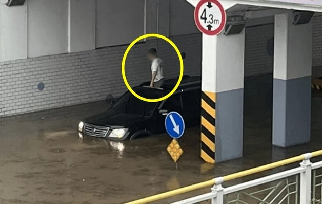 A man is seen standing out of the sunroof of a partially submerged vehicle. (Online community)