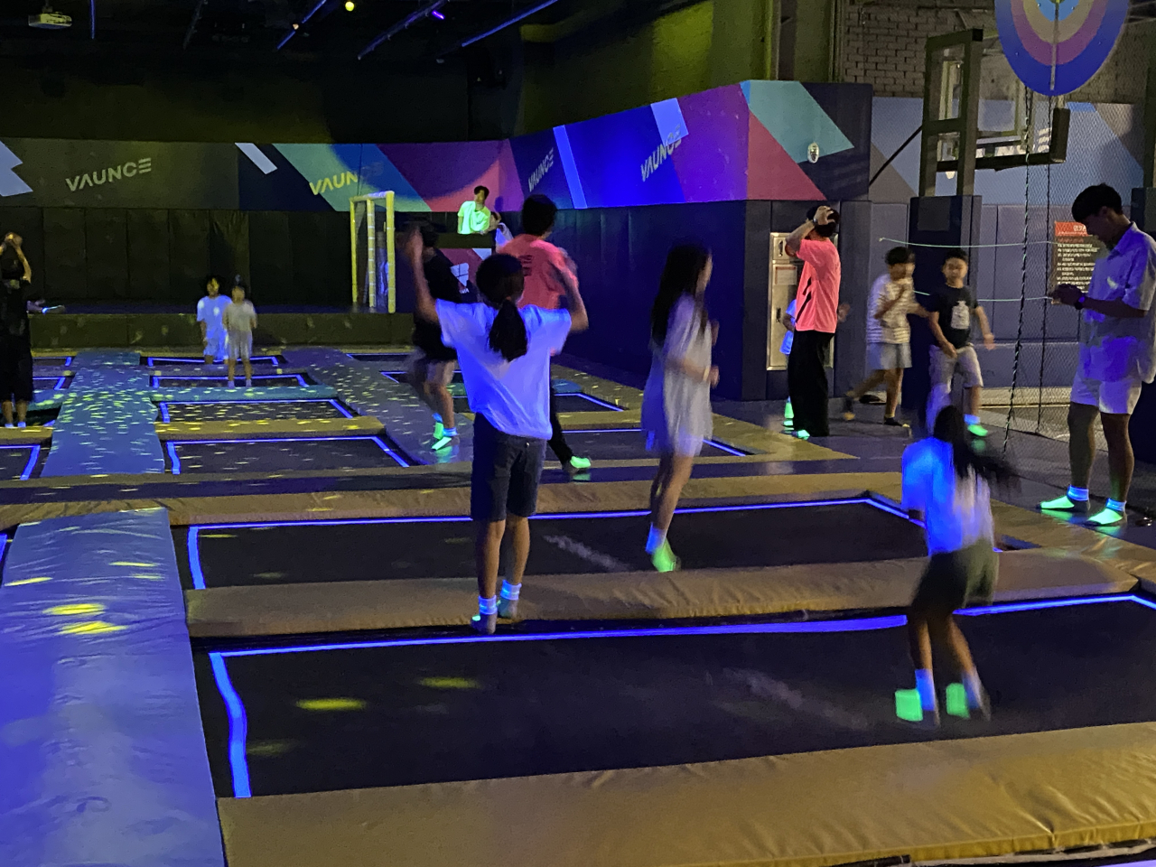Grown-ups and children alike bounce on trampolines under neon laser lights. (Hwang Joo-young/The Korea Herald)