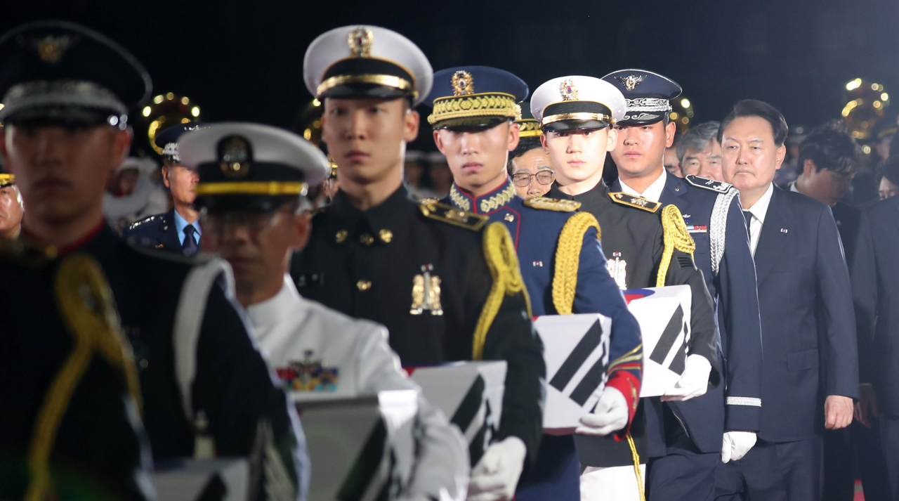 Soldiers carry coffins containing remains of seven South Korean soldiers killed during the Korean War in 1950-53, as President Yoon Suk Yeol (right) follow the soldiers during the ceremony held Wednesday at Seoul Air Base in Seongnam, Gyeonggi Province. (Presidential Office)