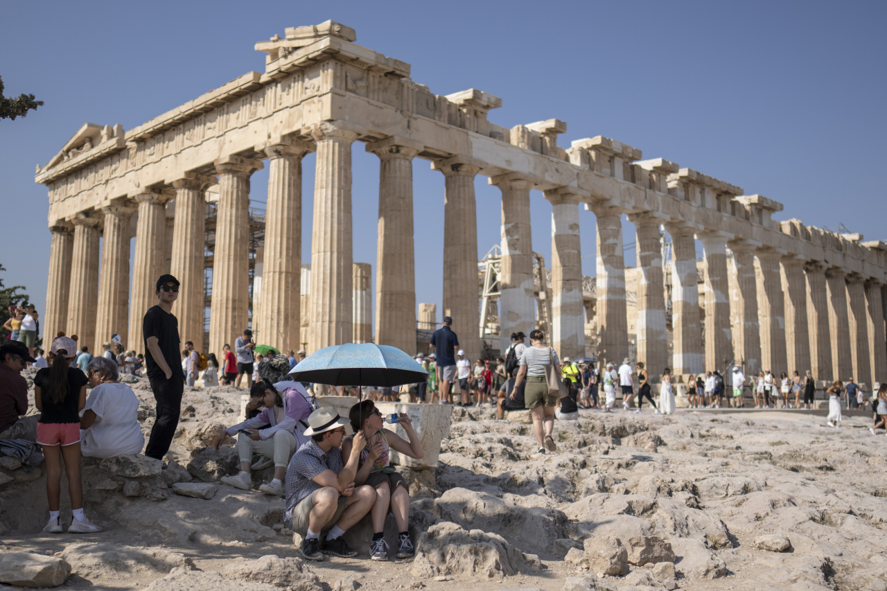 A tourist drinks water as she and a man sit under an umbrella in front of the five century BC Parthenon temple at the Acropolis hill during a heat wave, on July 13, 2023. (AP-Yonhap)