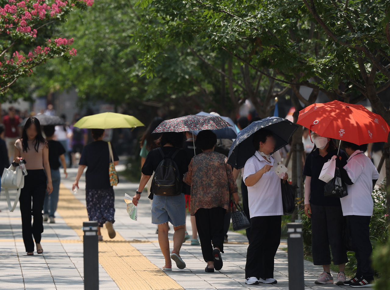 Amid the scorching weather nationwide, people carry parasols near the Gwanghwamun intersection in Seoul. (Yonhap)