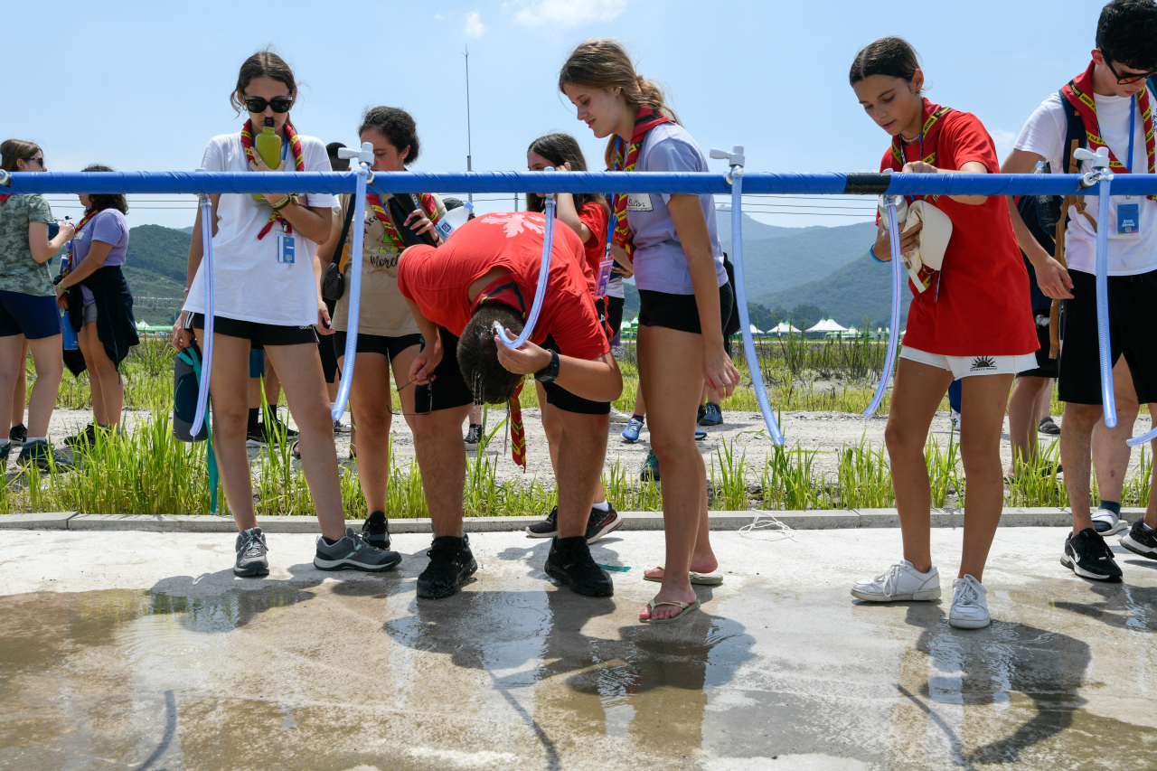 Scout members who participated in the 2023 World Scout Jamboree use water pump to endure the scorching weather, Tuesday. (WSBureau Inc./Jean-Pierre POUTEAU)