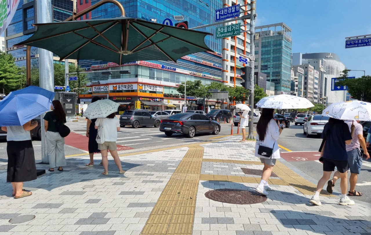 People holding umbrellas are waiting at a crosswalk in Seo-gu, Daejeon, on Aug. 5. (Yonhap)