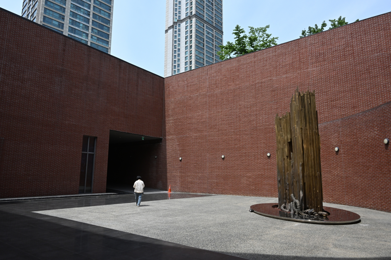 A visitor walks to the gate toward the museum entrance. On the right is an installation 