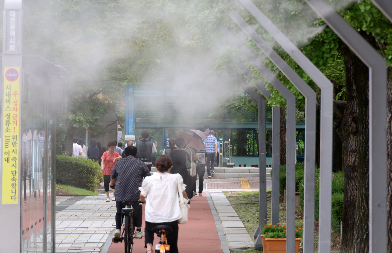 Citizens pass under a fog spray facility to cool the air installed in front of Daejeon City Hall in Seo-gu, Daejeon on Tuesday afternoon. (Yonhap)