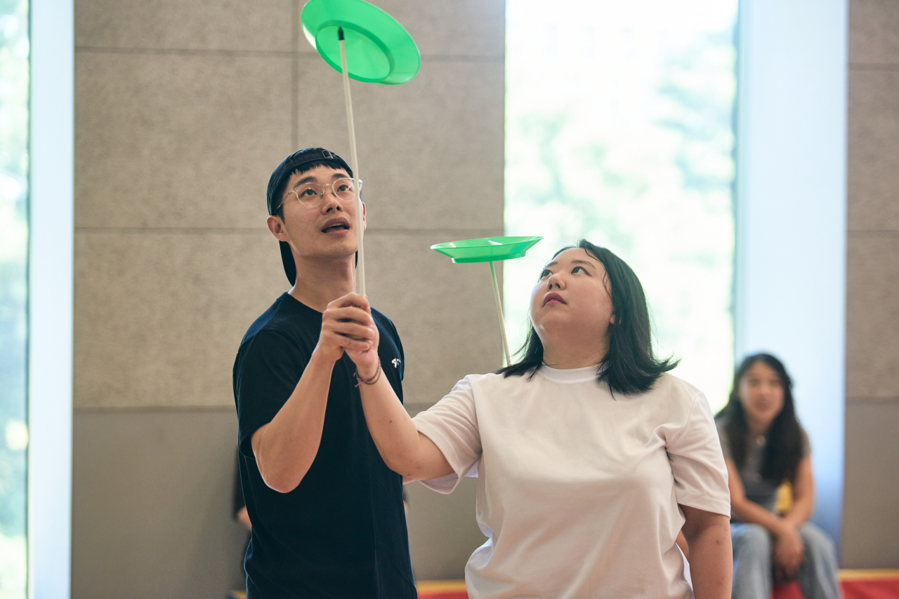 A participant tries out plate spinning while an instructor assists her during a 