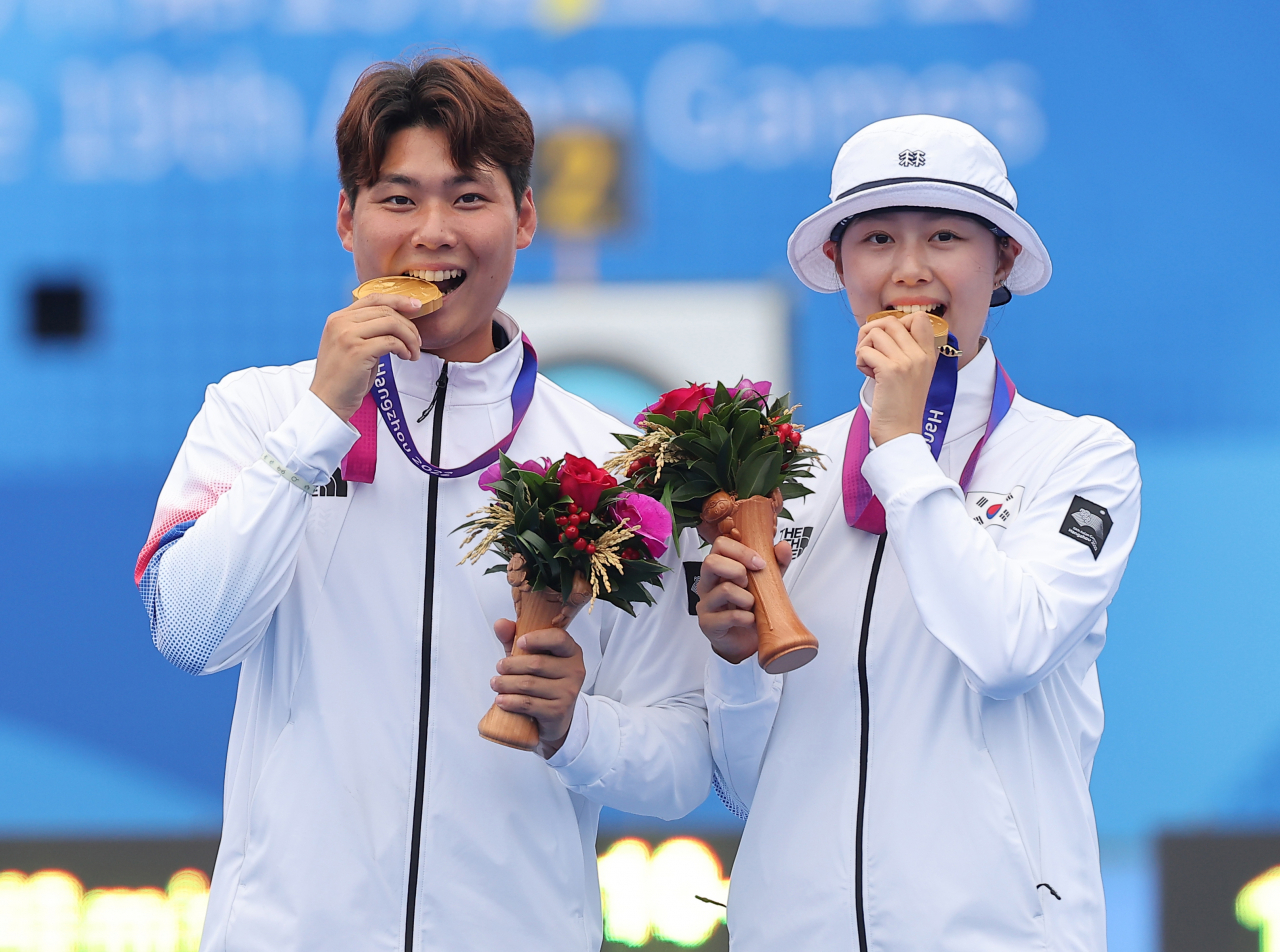 South Korean archers Lee Woo-seok (left) and Lim Si-hyeon bite their gold medals during the medal ceremony for the recurve mixed team event at the Asian Games at the Fuyang Yinhu Sports Center in Hangzhou, China, Wednesday. (Yonhap)
