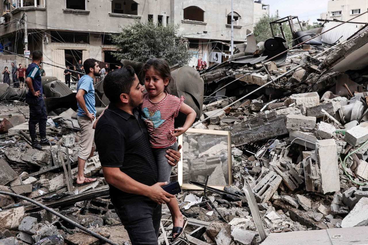 A man carries a crying child as he walks in front of a building destroyed in an Israeli air strike in Gaza City on Saturday (local time). (AFP-Yonhap)