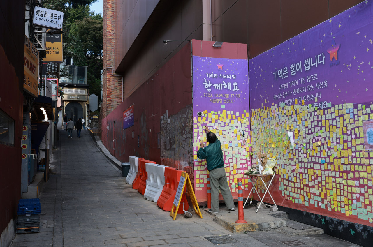 A man puts a mourning message for victims of the 2022 deadly crowd crush in Seoul's Itaewon on a board set up at the site of the accident on Oct. 15, ahead of the tragedy's first anniversary. (Yonhap)