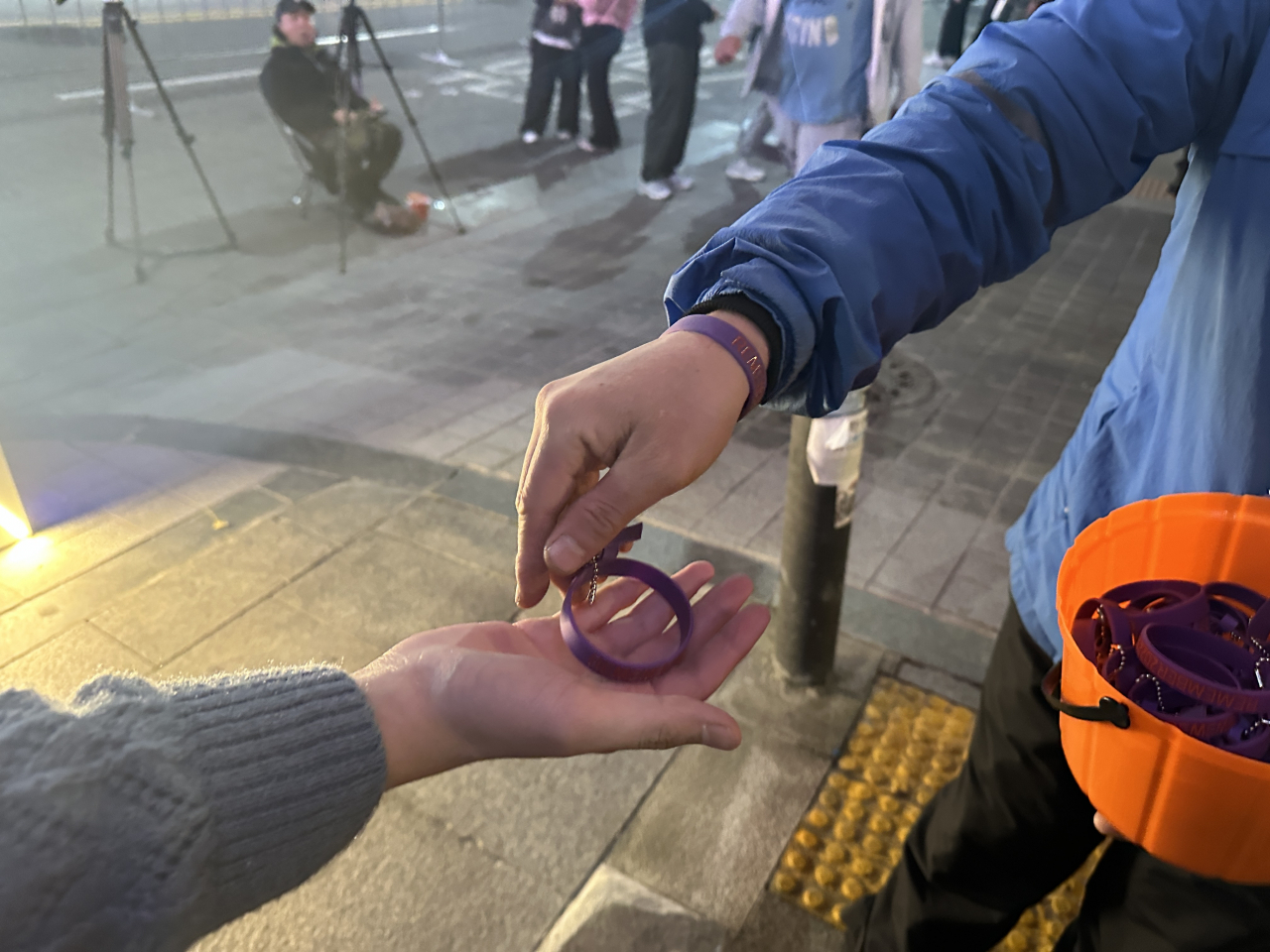 A volunteer from the Itaewon Disaster Citizens’ Task Force and Itaewon Disaster Bereaved Families hand out purple ribbons and bracelets to a passerby at Itaewon on Oct. 28. (Lee Jung-joo/The Korea Herald)