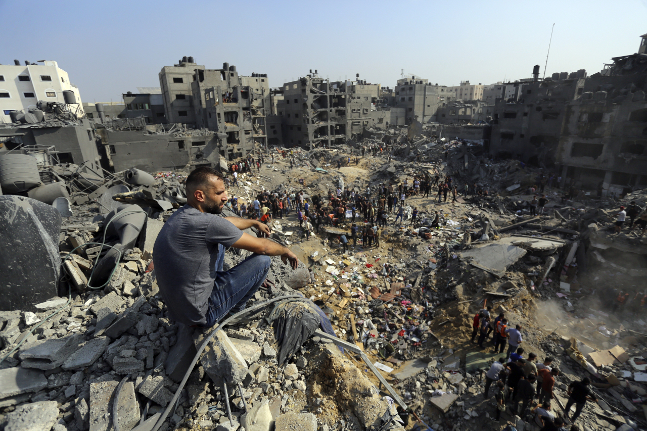 A man sits on the rubble as others wander among debris of buildings that were targeted by Israeli airstrikes in Jabaliya refugee camp, northern Gaza Strip, Wednesday (AP-Yonhap)