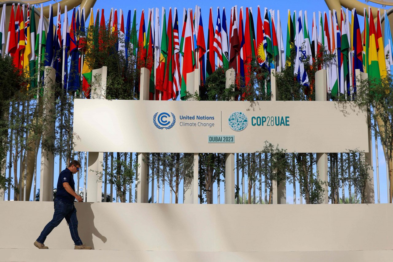 A man walks past national flags of participating countries at the venue of the COP28 United Nations climate summit in Dubai on Thursday. The UN climate conference opens in Dubai on Thursday with nations under pressure to increase the urgency of action on global warming and wean off fossil fuels, amid intense scrutiny of oil-rich hosts UAE. (AFP)