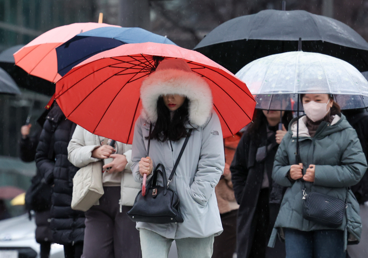 People hold on to their umbrellas amid rain in downtown Seoul on Friday. (Newsis)