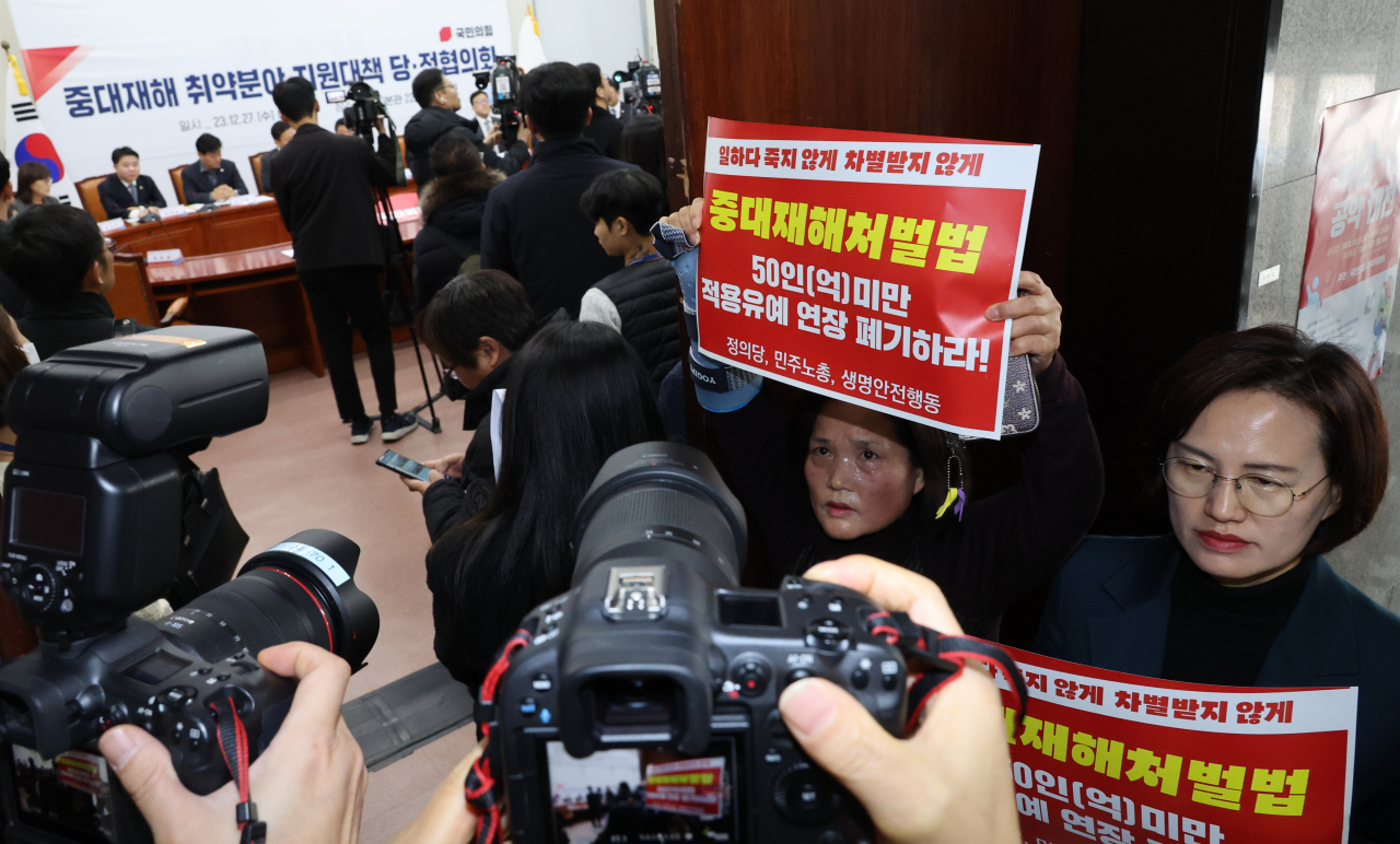 Protesters hold placards Wednesday in front of a meeting room at the National Assembly where officials of the government and the ruling People Power Party lawmakers agreed to defer the enforcement of the Serious Disasters Punishments Act. (Yonhap)
