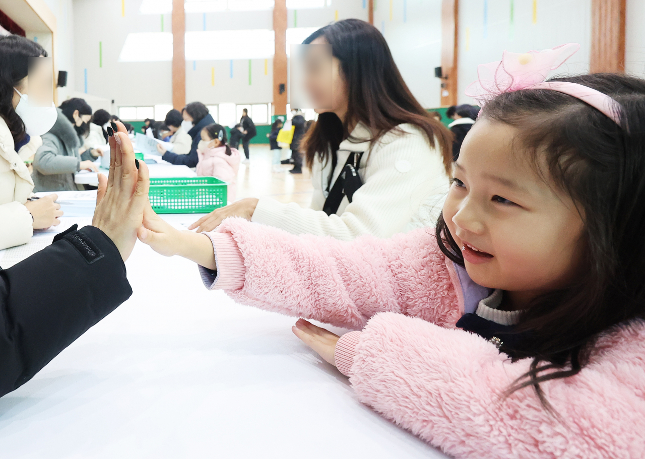 A child is greeted by a teacher at an orientation day for new students at Yeongdeok Elementary School in Suwon, Gyeonggi Province, Dec. 26. (Yonhap)